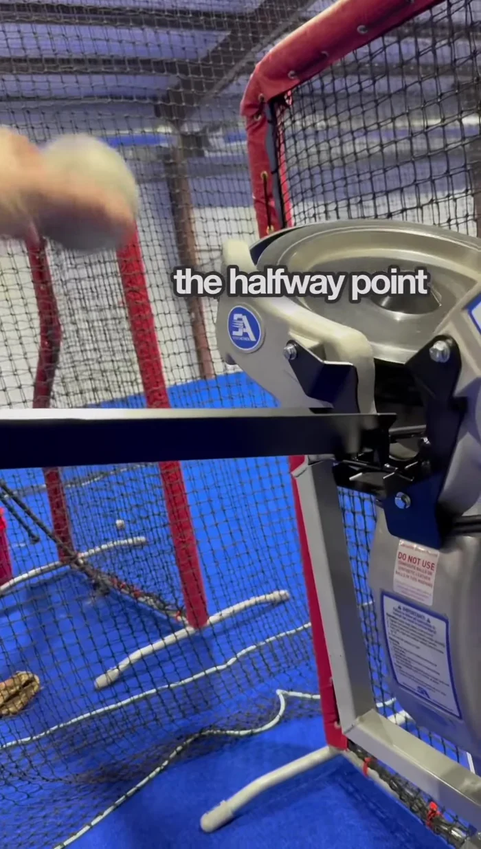 Feed the ball, aiming for a four-seam grip and a smooth roll into the machine's feeding mechanism (around the halfway point of the feeder).