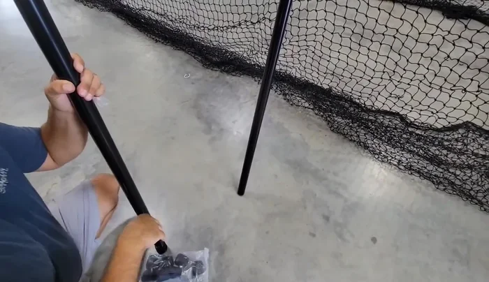 With assistance, lift the frame and attach the remaining poles to complete the 10ft height. Use bungee cords to secure the net to the crossbars for easier handling.