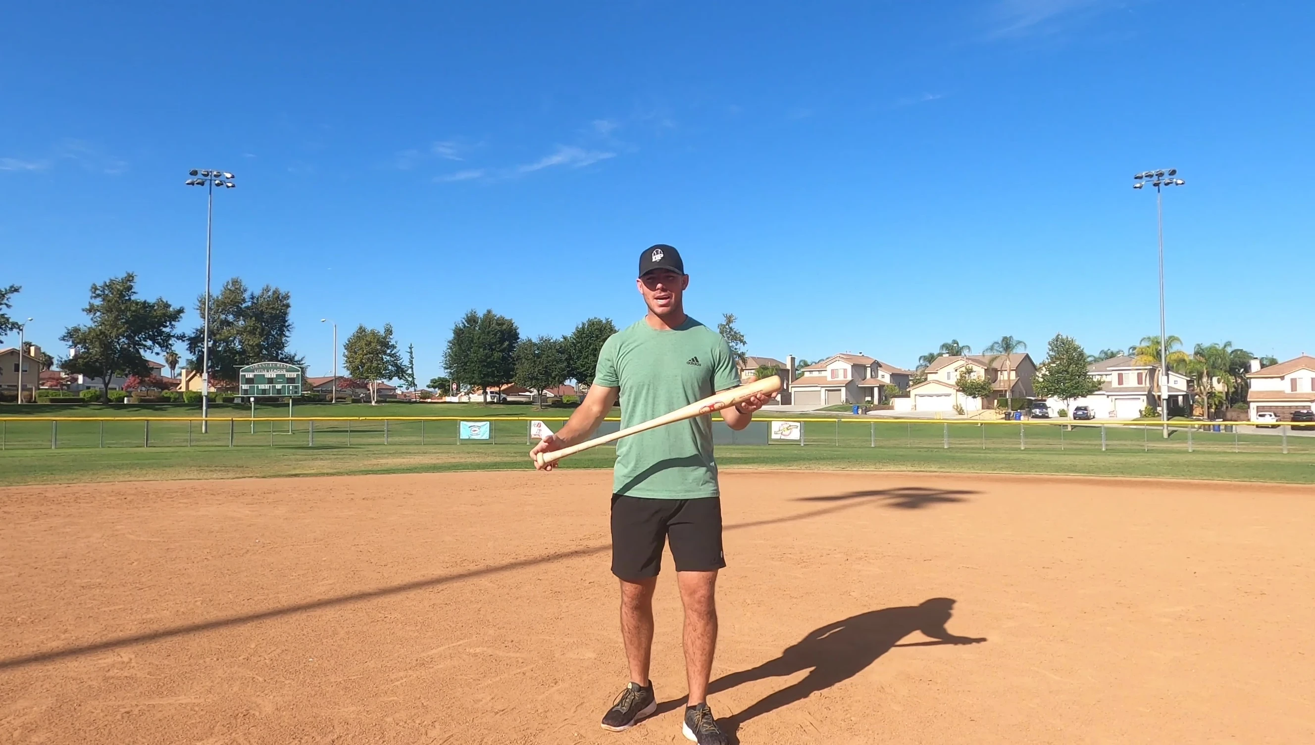 Five young baseball players practicing the bat-throwing drill in a park.